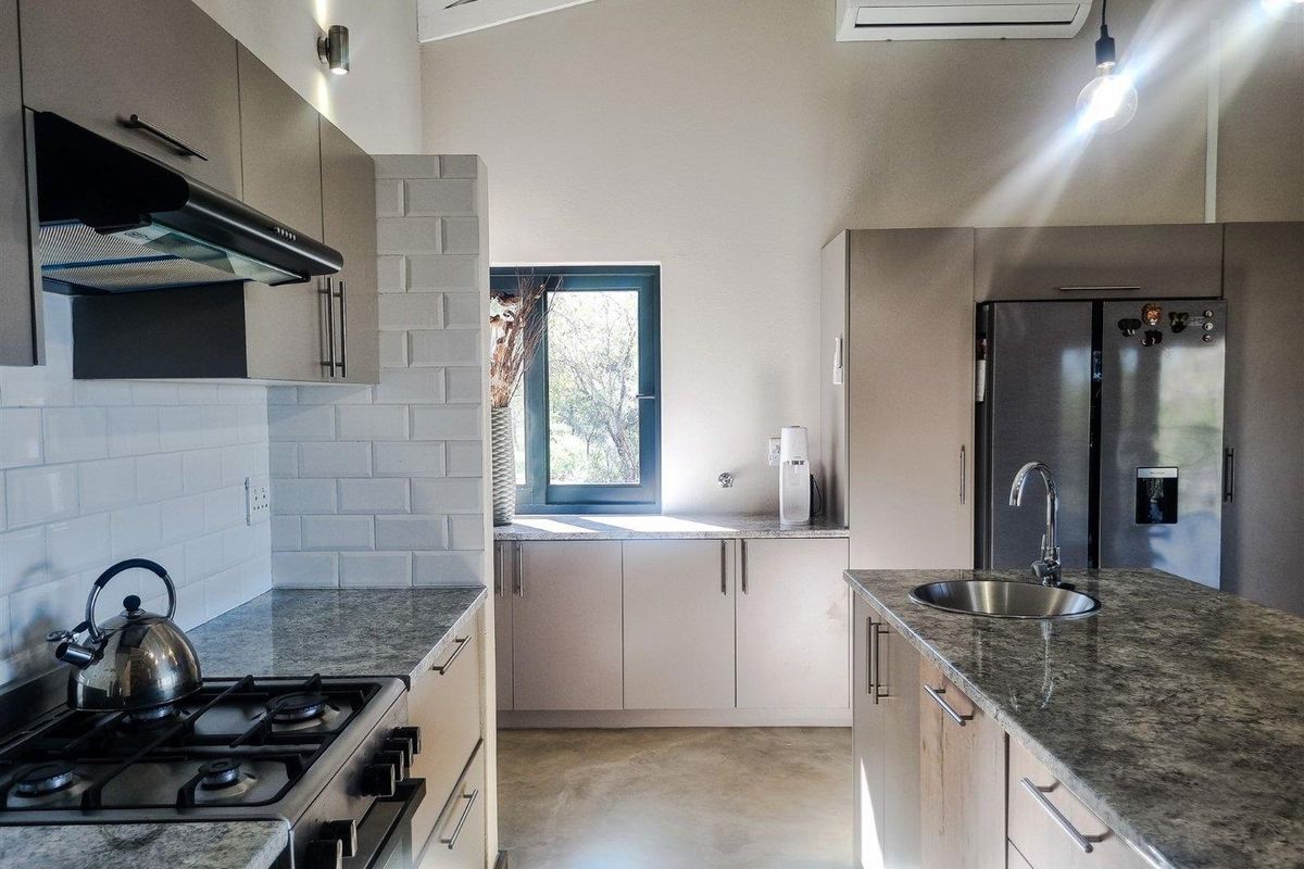 Modern kitchen featuring stone countertops, subway tile backsplash, gas stove, extractor fan, and a central island with a stainless steel sink.