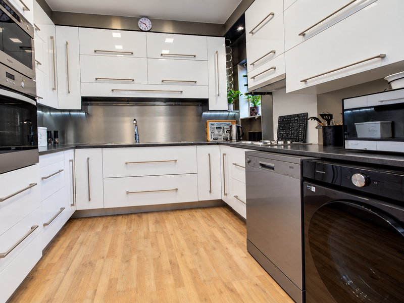 Modern kitchen featuring high-gloss white cabinetry, stainless steel appliances, integrated dishwasher, and durable laminate flooring with a sleek stainless steel splashback.
