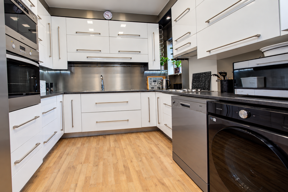 Modern kitchen featuring high-gloss white cabinetry, stainless steel appliances, integrated dishwasher, and durable laminate flooring with a sleek stainless steel splashback.