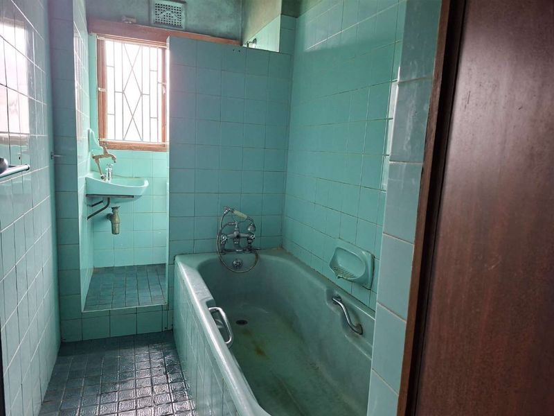 A dated bathroom featuring original blue ceramic tiling, a built-in bathtub, and a wall-mounted basin, requiring modernization and renovation.