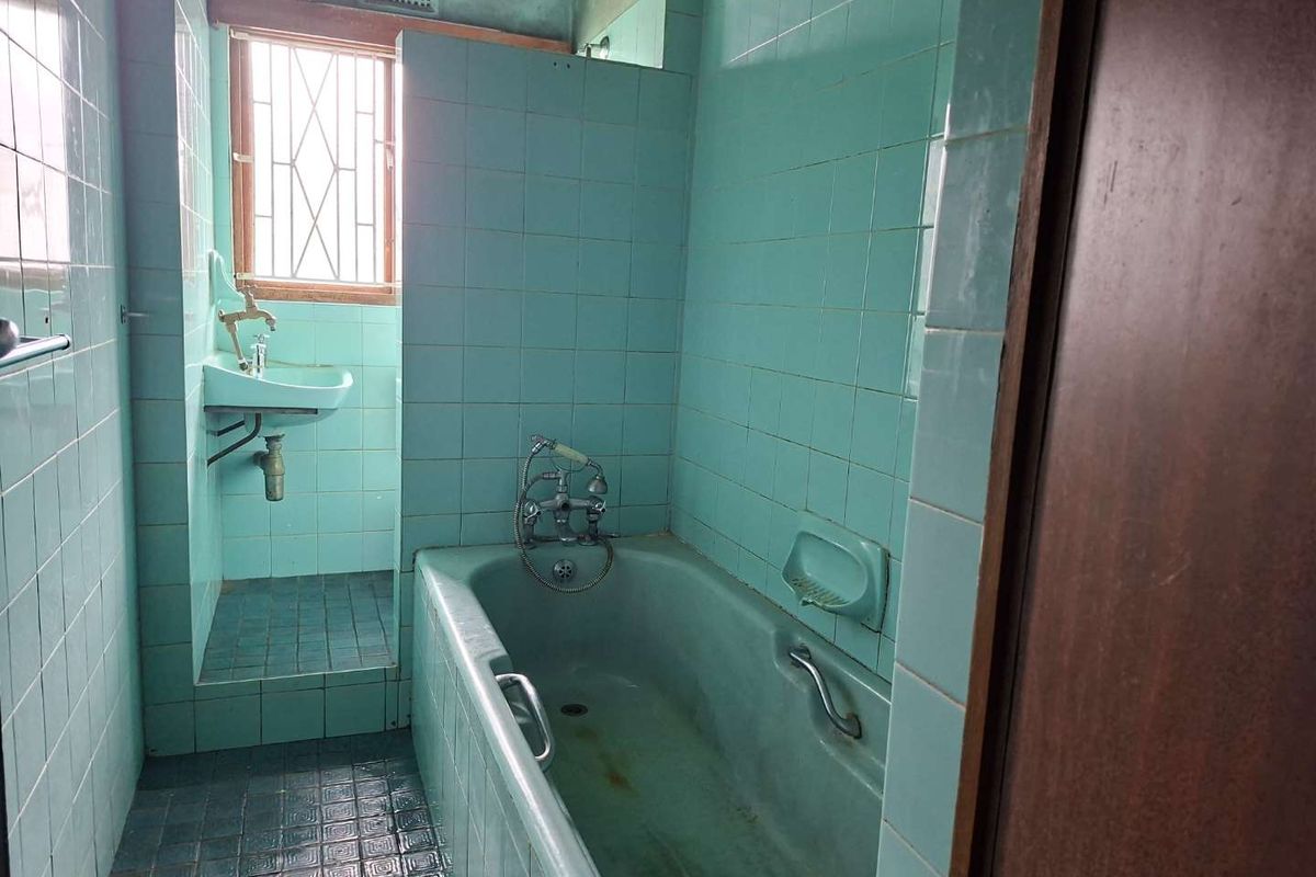 A dated bathroom featuring original blue ceramic tiling, a built-in bathtub, and a wall-mounted basin, requiring modernization and renovation.