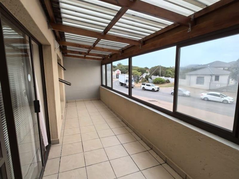 A covered balcony featuring tiled flooring, a timber pergola roof with polycarbonate sheeting, and large glass windows overlooking the street.