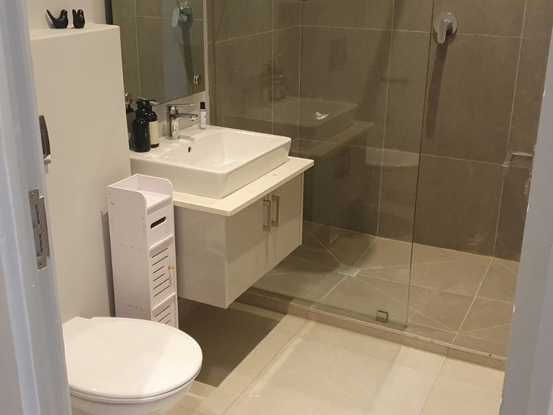 Modern bathroom featuring a wall-mounted vanity with a ceramic basin, a glass-enclosed shower with tiled walls, and contemporary fixtures.