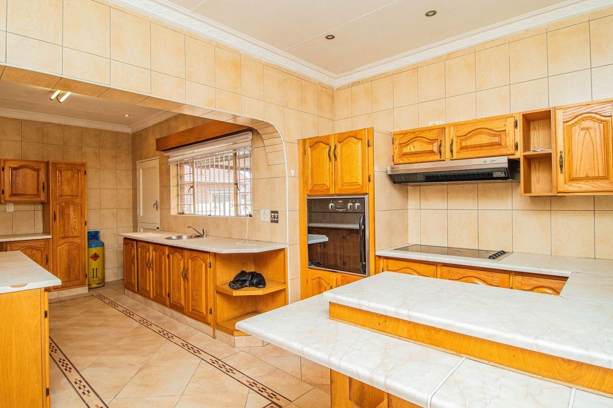 Spacious kitchen featuring wooden cabinetry, built-in oven, extractor fan, and tiled countertops with an integrated sink and breakfast bar area.