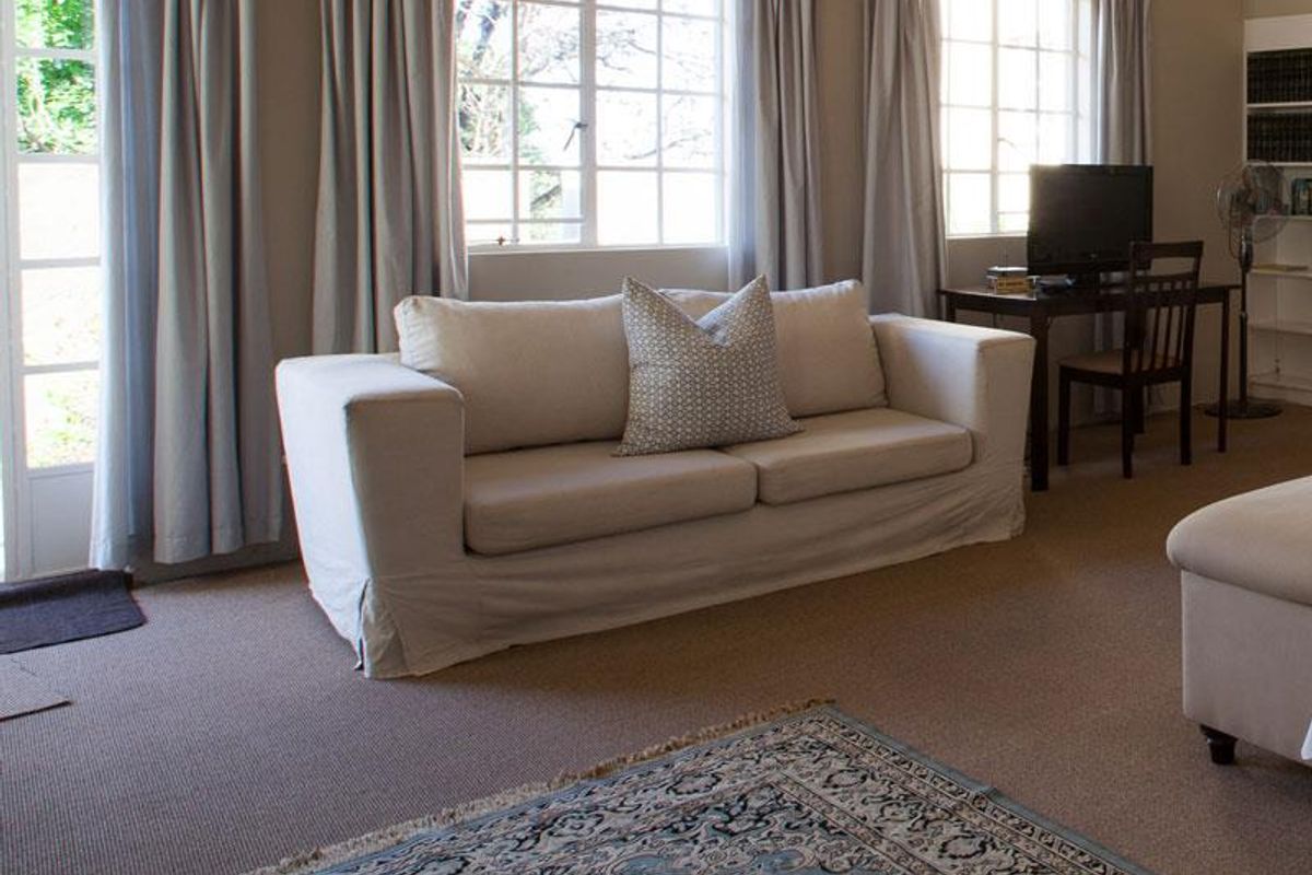 A comfortable living room featuring large windows with natural light, neutral carpeting, and built-in shelving units.