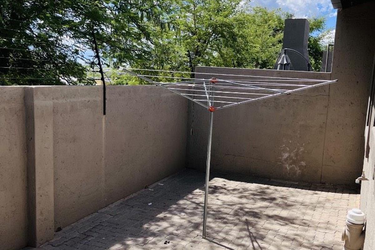 A paved rear courtyard area featuring a boundary wall with electric fencing and an outdoor water connection point.