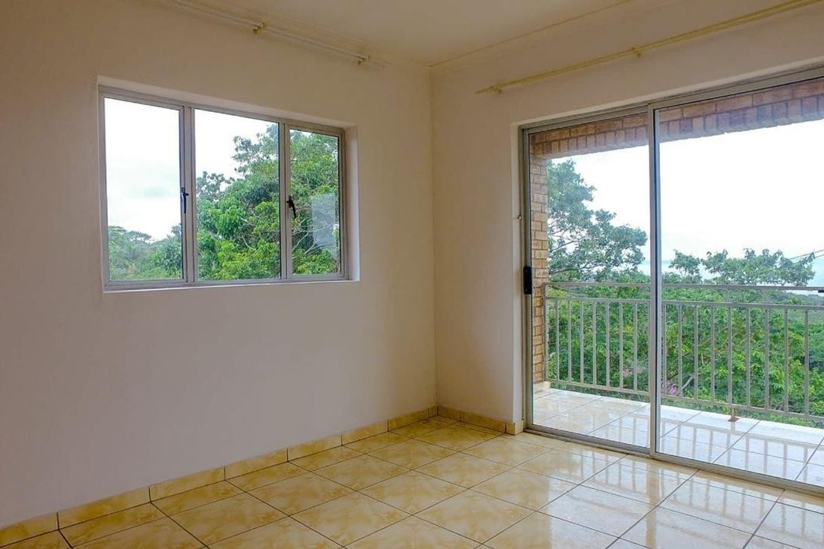 An empty bedroom featuring tiled flooring, aluminium window frames, and a sliding door leading to a private balcony with scenic views.