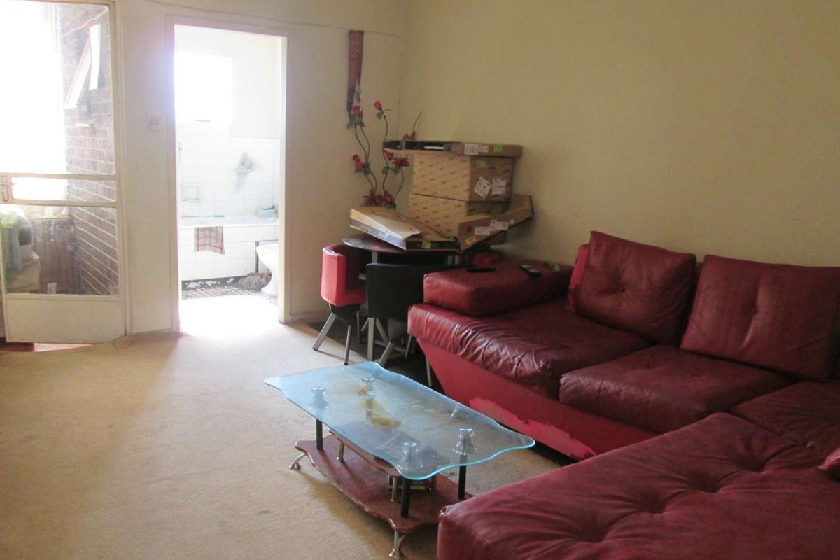 A living room area featuring carpet flooring and access to an adjacent bathroom, requiring cosmetic updates to improve the overall condition.