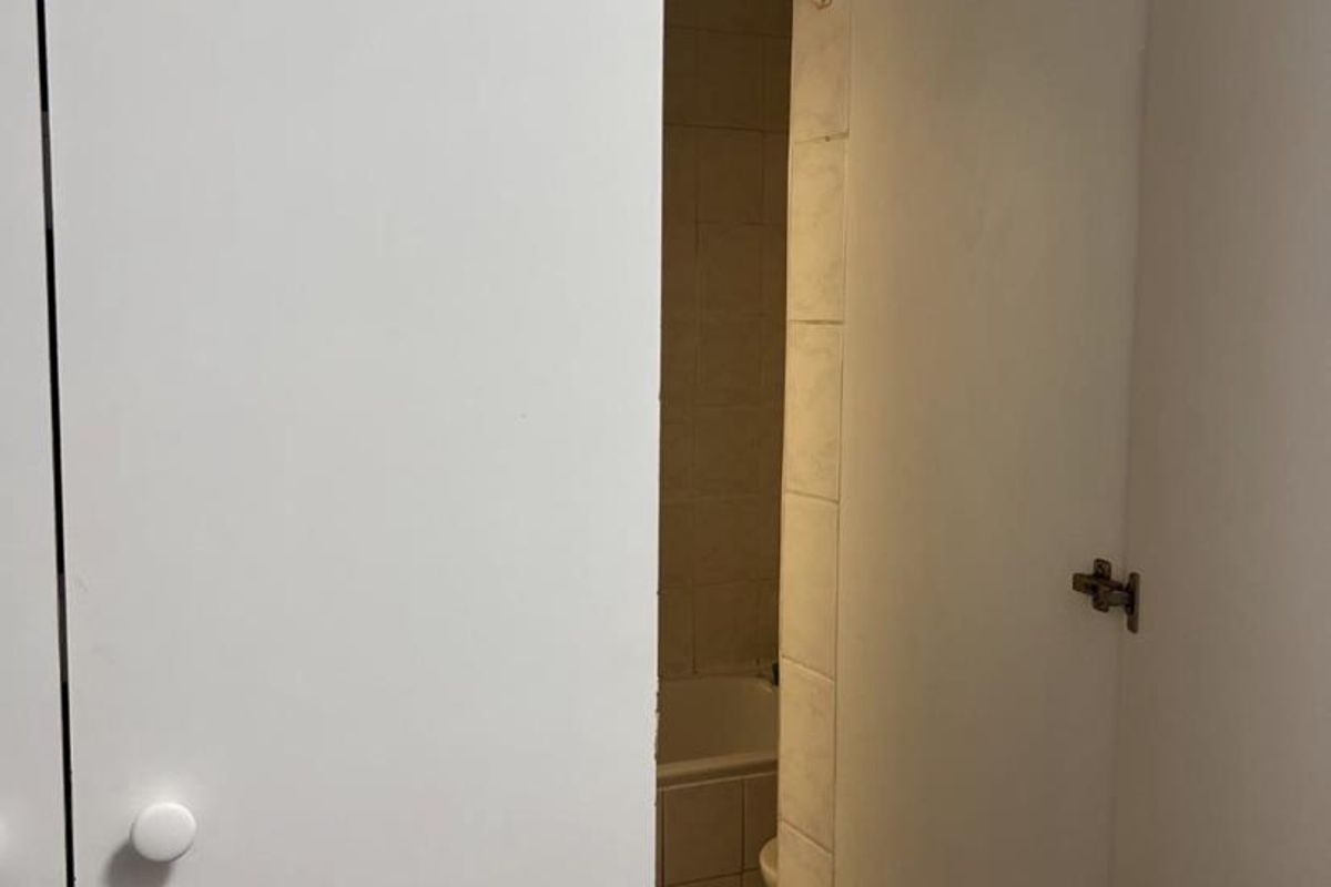 A view through a partially open door into a bathroom featuring tiled walls, tiled flooring, and a built-in bathtub.