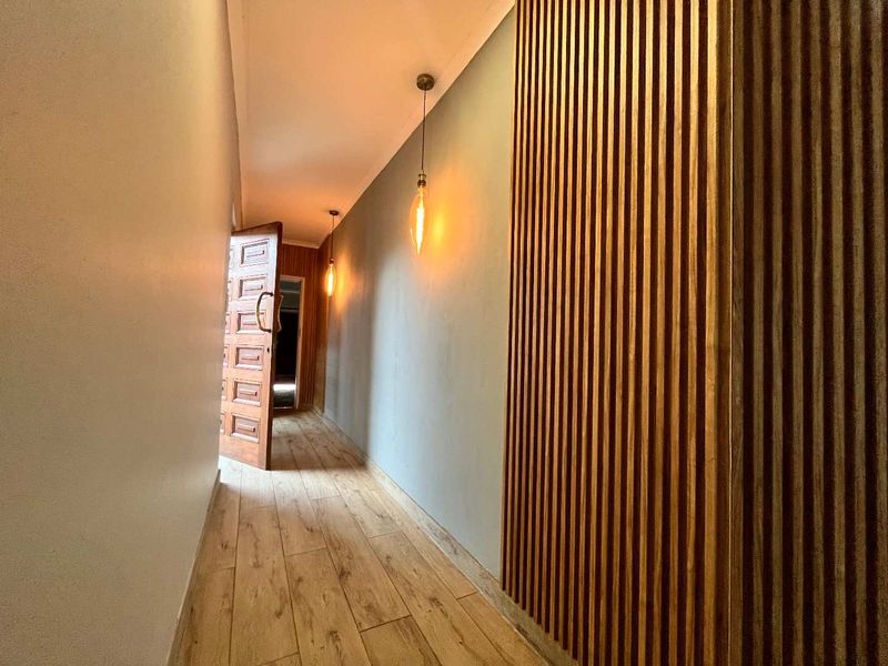 A modern hallway featuring stylish timber slat wall paneling, warm pendant lighting, and durable wood-look tile flooring.