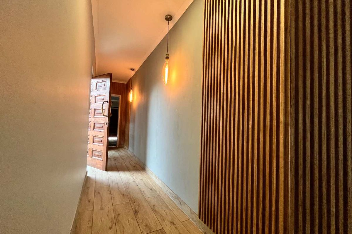 A modern hallway featuring stylish timber slat wall paneling, warm pendant lighting, and durable wood-look tile flooring.
