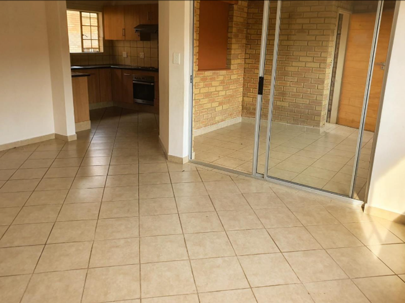 Open-plan living area featuring ceramic tiled flooring, a functional kitchen with built-in appliances, and a sliding glass door leading to an enclosed brick-walled space.