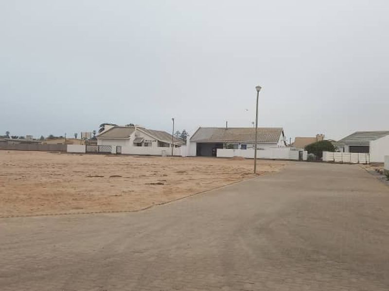 A street view showing a paved road, boundary walls, and surrounding residential properties in a quiet neighborhood setting.
