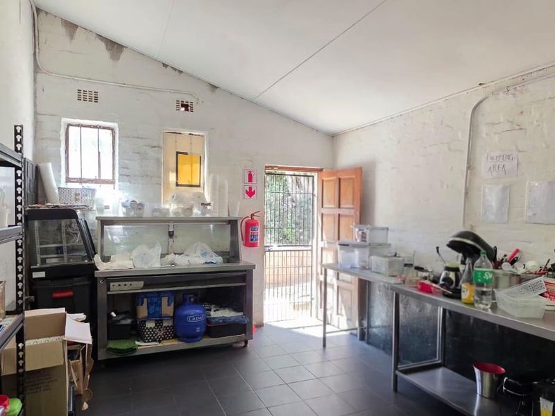 Functional commercial scullery or prep area featuring tiled floors, stainless steel work surfaces, and direct access to an exterior security gate.