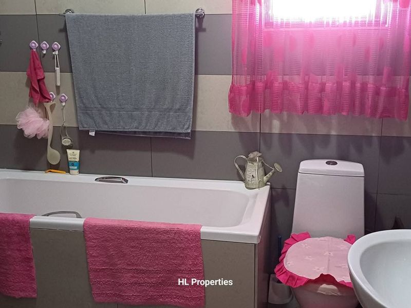 A functional bathroom featuring a bathtub with shower mixer, a standard toilet, and a pedestal basin with tiled wall finishes.