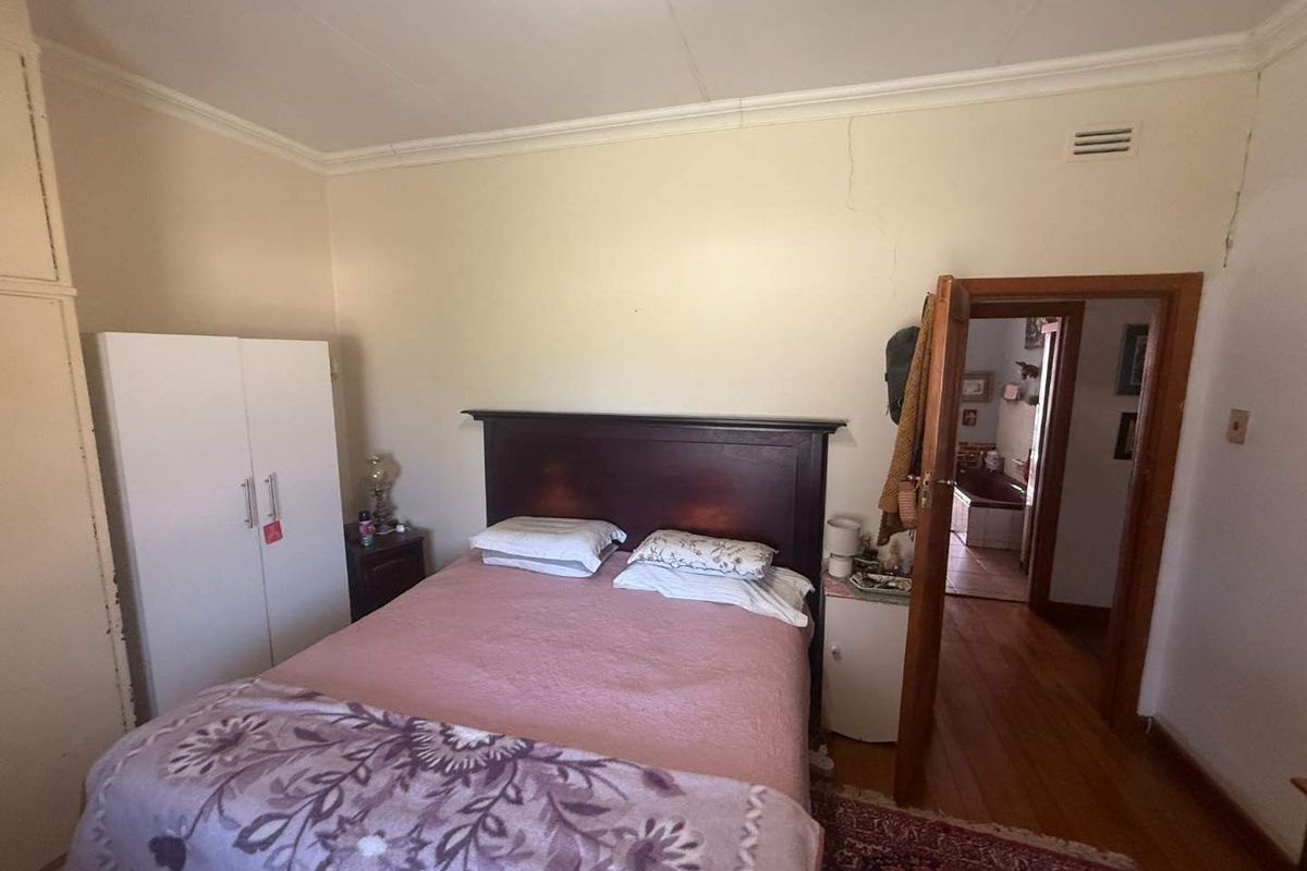 A bedroom featuring hardwood flooring, built-in wardrobe, and direct access to an adjoining bathroom, showing signs of wall cracking.