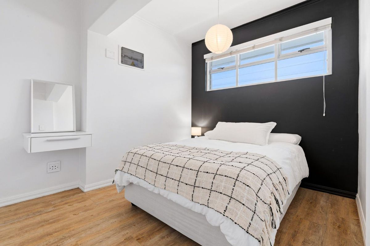 A modern bedroom featuring wood-look flooring, a floating vanity shelf, and a striking black accent wall with a horizontal window.
