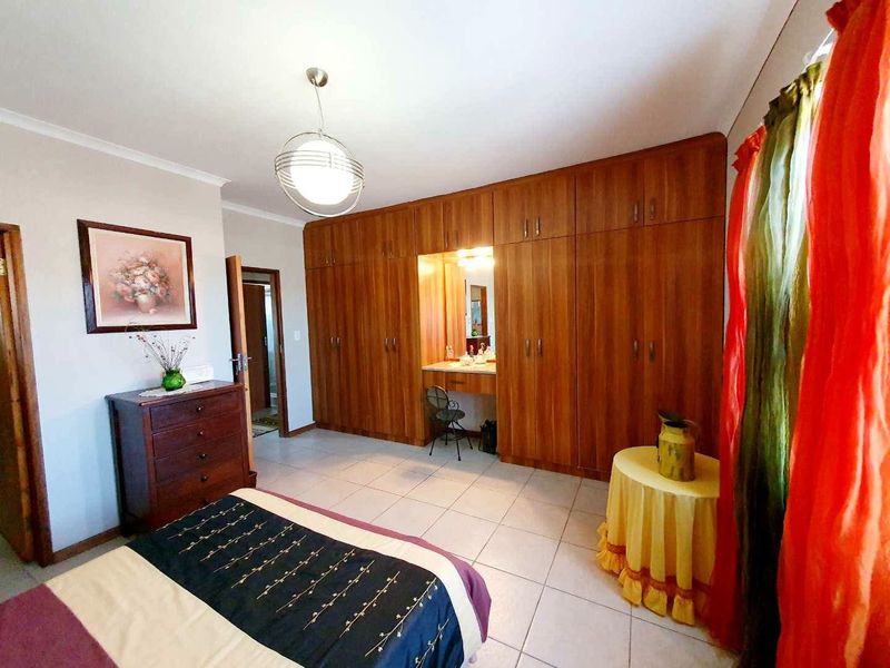 Spacious bedroom featuring extensive built-in wooden cabinetry with an integrated vanity station and neutral tiled flooring.