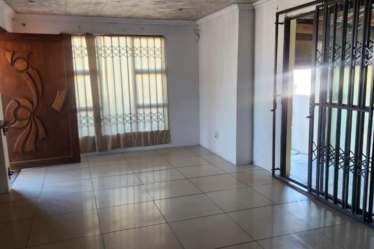 An empty living area featuring tiled flooring, a textured ceiling, and security gates leading to an outdoor space.