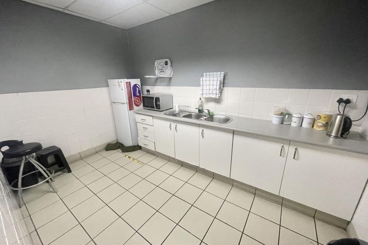 A functional industrial kitchenette featuring white cabinetry, a stainless steel sink, tiled splashback, and durable floor tiles.
