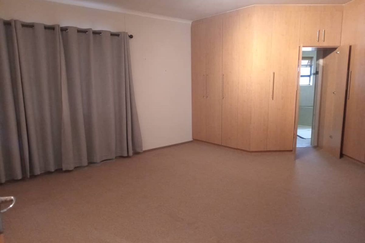 Spacious bedroom featuring extensive built-in wooden cupboards, neutral carpeting, and direct access to an en-suite bathroom.