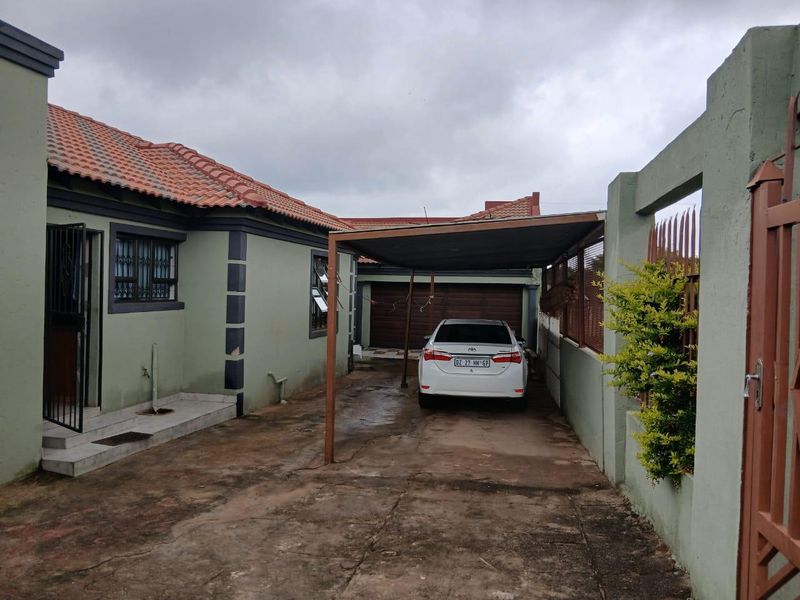 Exterior view of the property featuring a paved driveway, a covered carport, and a secure perimeter wall with gated access.