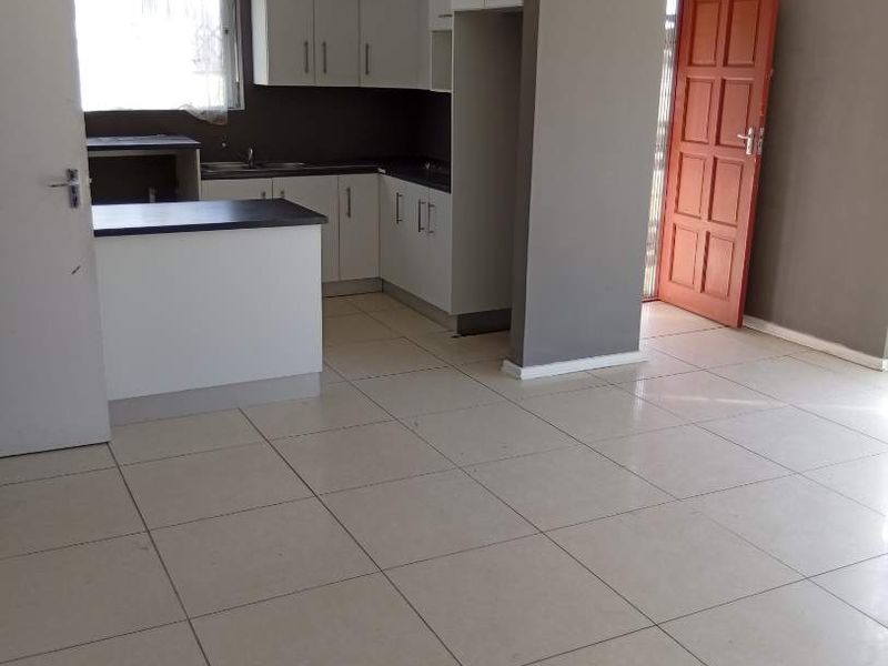 An open-plan living and kitchen area featuring neutral tiled flooring, modern white cabinetry, and a breakfast counter, providing a clean and versatile living space.