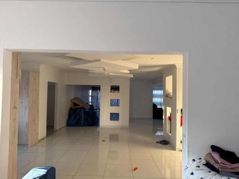 Spacious open-plan living area featuring tiled floors, decorative ceiling bulkheads, and built-in wall niches, offering a versatile layout for modern living.