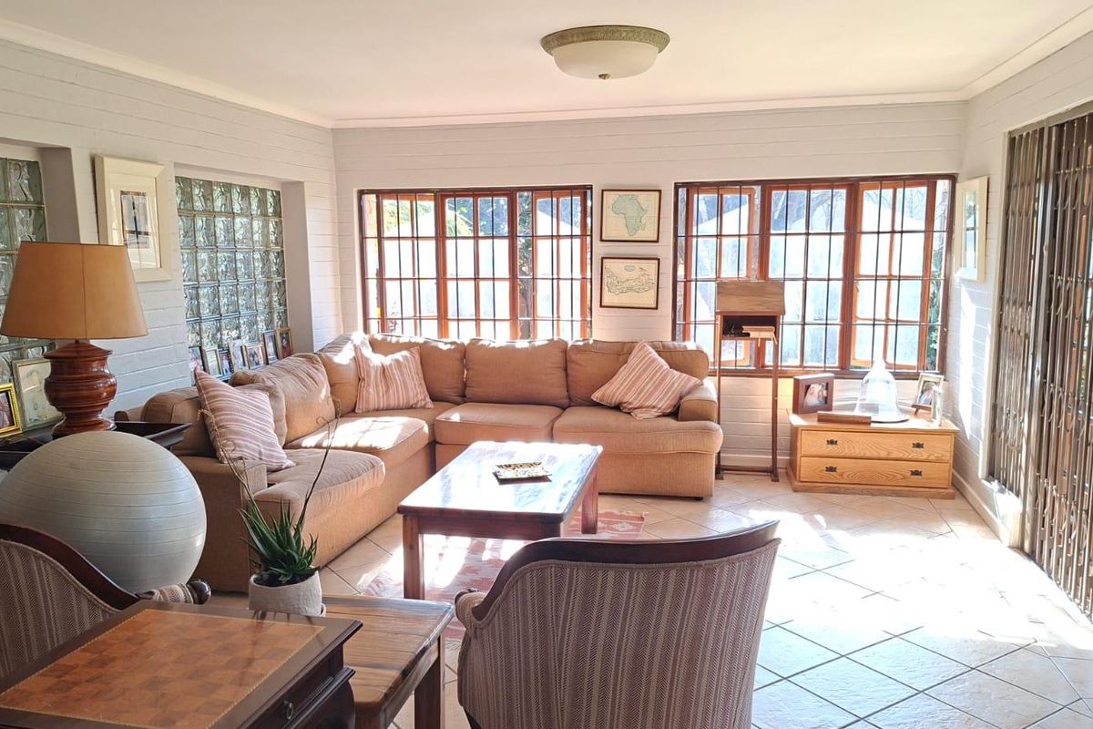 A bright living room featuring tiled flooring, glass block feature wall, and large timber-framed windows allowing for ample natural light.