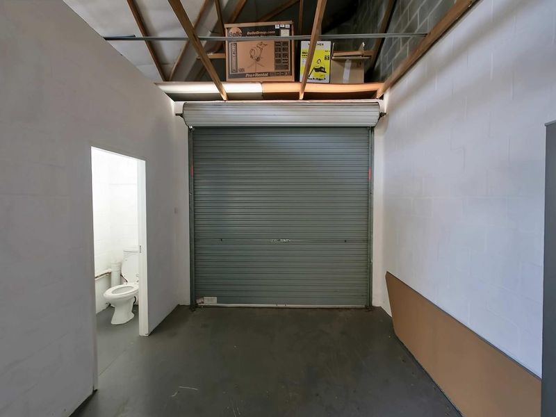 Industrial garage space featuring a roller shutter door, exposed roof trusses, and an integrated private toilet facility.