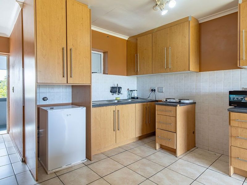 A functional kitchen featuring laminate cabinetry, tiled backsplash, and ceramic flooring, with direct access to an outdoor balcony area.