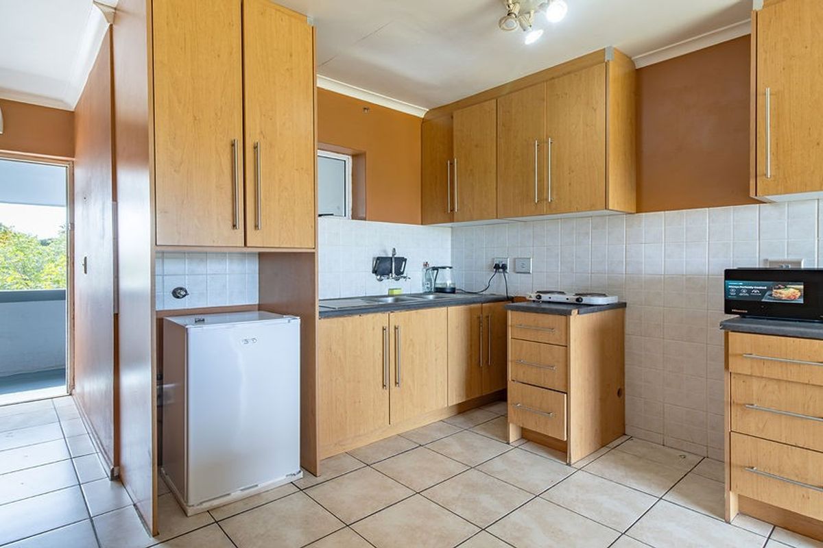 A functional kitchen featuring laminate cabinetry, tiled backsplash, and ceramic flooring, with direct access to an outdoor balcony area.
