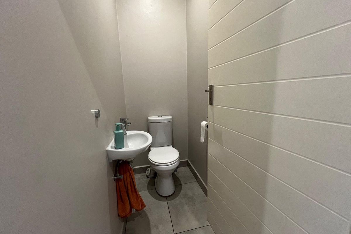 A compact guest cloakroom featuring a wall-mounted basin, a modern toilet, and tiled flooring, accessed via a horizontal panel door.
