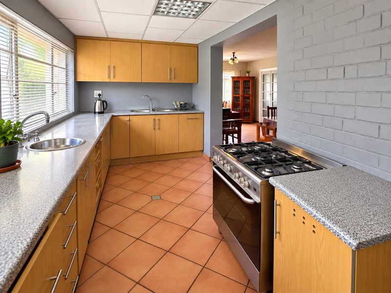 Functional kitchen featuring light wood cabinetry, granite-look countertops, a gas stove, and terracotta floor tiles, with an open-plan flow to the dining area.