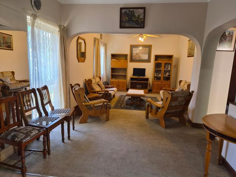 A spacious living room featuring an arched entryway, ceiling fan, and carpeted flooring, offering a comfortable and traditional layout.