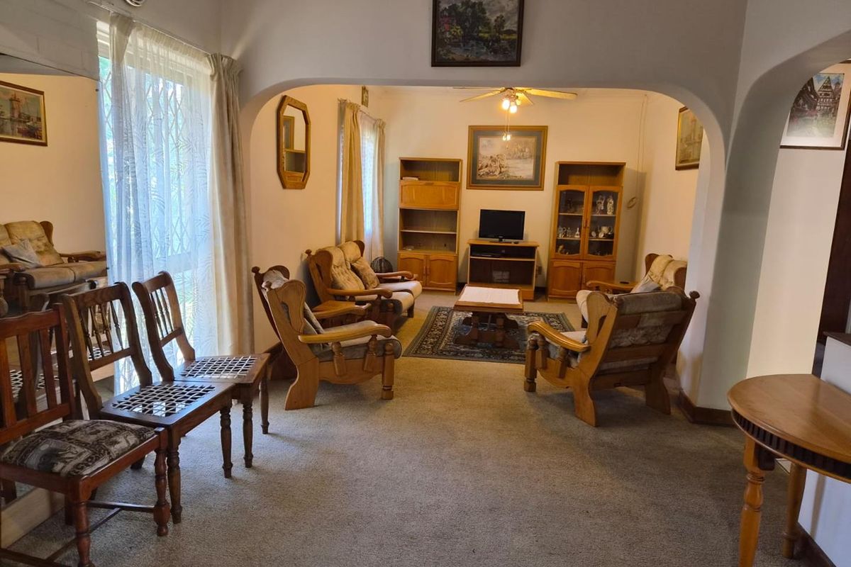 A spacious living room featuring an arched entryway, ceiling fan, and carpeted flooring, offering a comfortable and traditional layout.
