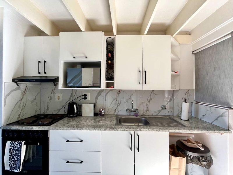 A compact, modern kitchen featuring white cabinetry, marble-look backsplash, granite-style countertops, and integrated appliances including an oven, hob, and extractor fan.
