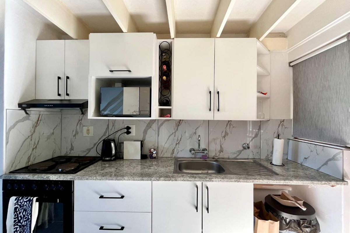 A compact, modern kitchen featuring white cabinetry, marble-look backsplash, granite-style countertops, and integrated appliances including an oven, hob, and extractor fan.