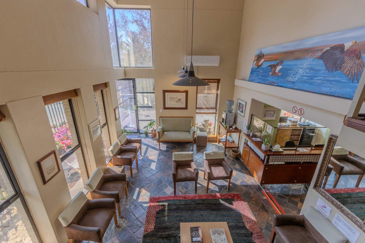 A spacious, double-volume living area featuring slate tile flooring, large windows for natural light, and a built-in reception counter.