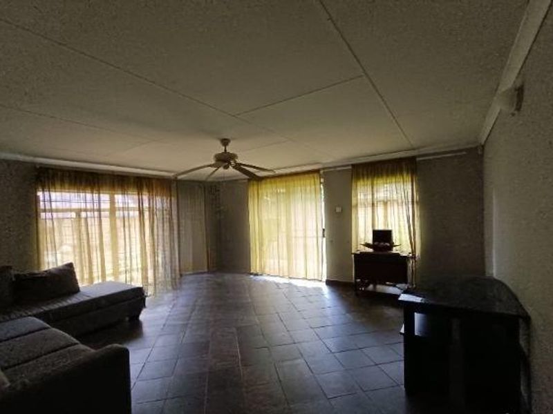 Spacious living area featuring tiled flooring, a ceiling fan, and large sliding glass doors providing ample natural light.
