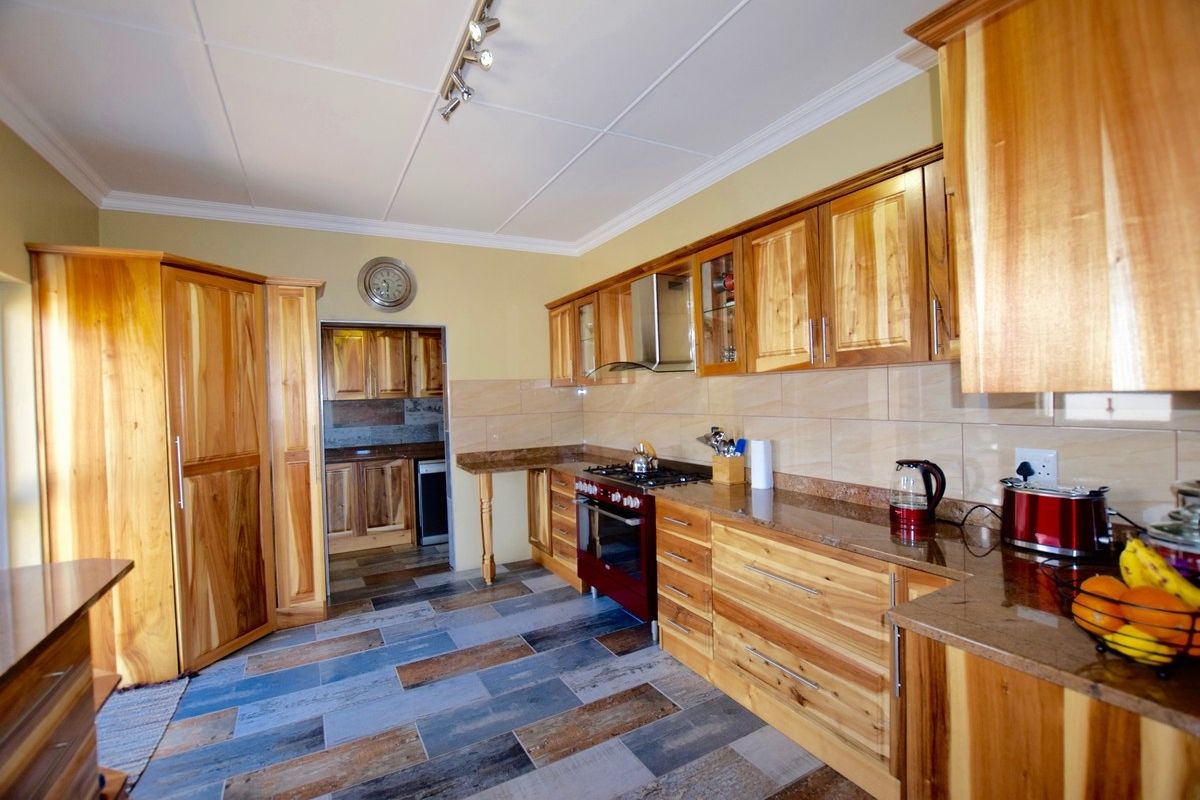 Spacious kitchen featuring natural wood cabinetry, granite countertops, tiled flooring, and a built-in gas stove with extractor fan, leading into a separate scullery area.