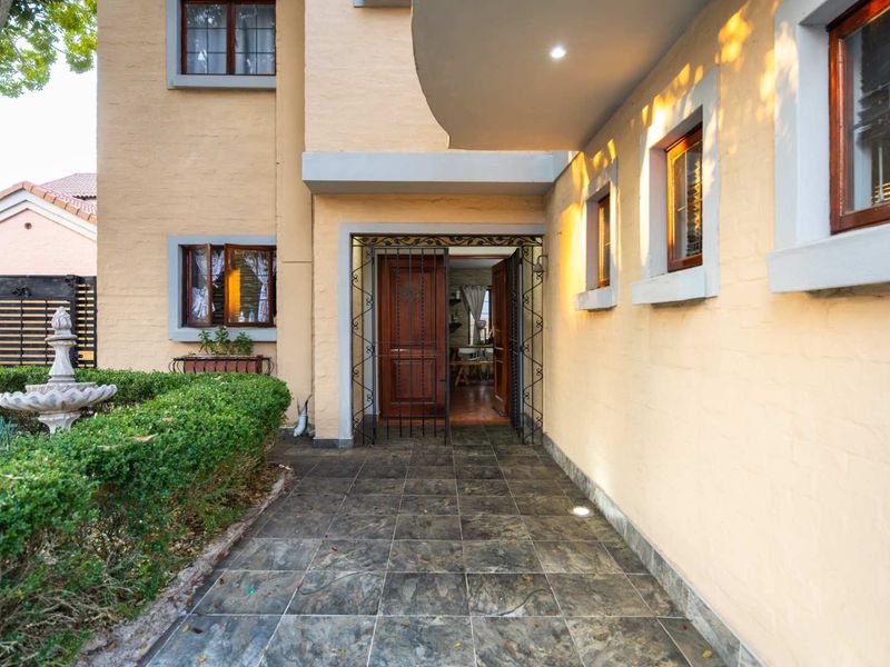 A welcoming front entrance featuring a tiled walkway, security gate, timber door, and a landscaped garden with a stone fountain.