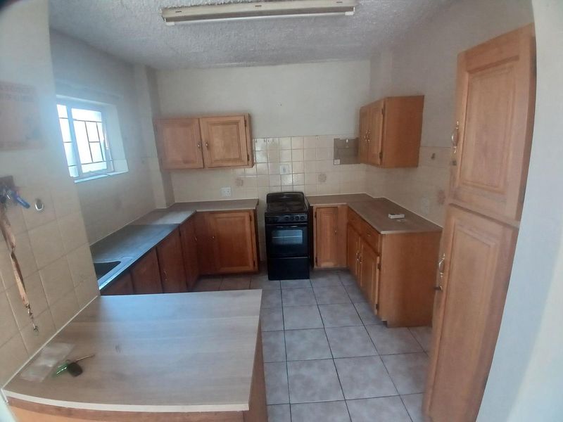 A dated kitchen featuring wooden cabinetry, tiled backsplash, and tiled flooring. The space is empty and ready for a modern renovation.