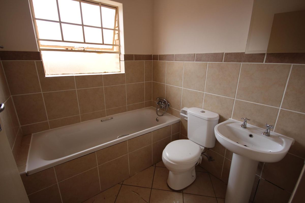 A functional bathroom featuring a built-in bathtub, pedestal basin, and toilet with neutral wall tiling and a window for natural light.