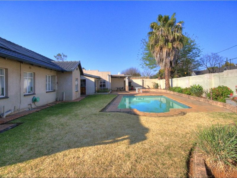 Rear garden area featuring a swimming pool with paved surround, lawn, and a covered patio attached to the main house structure.