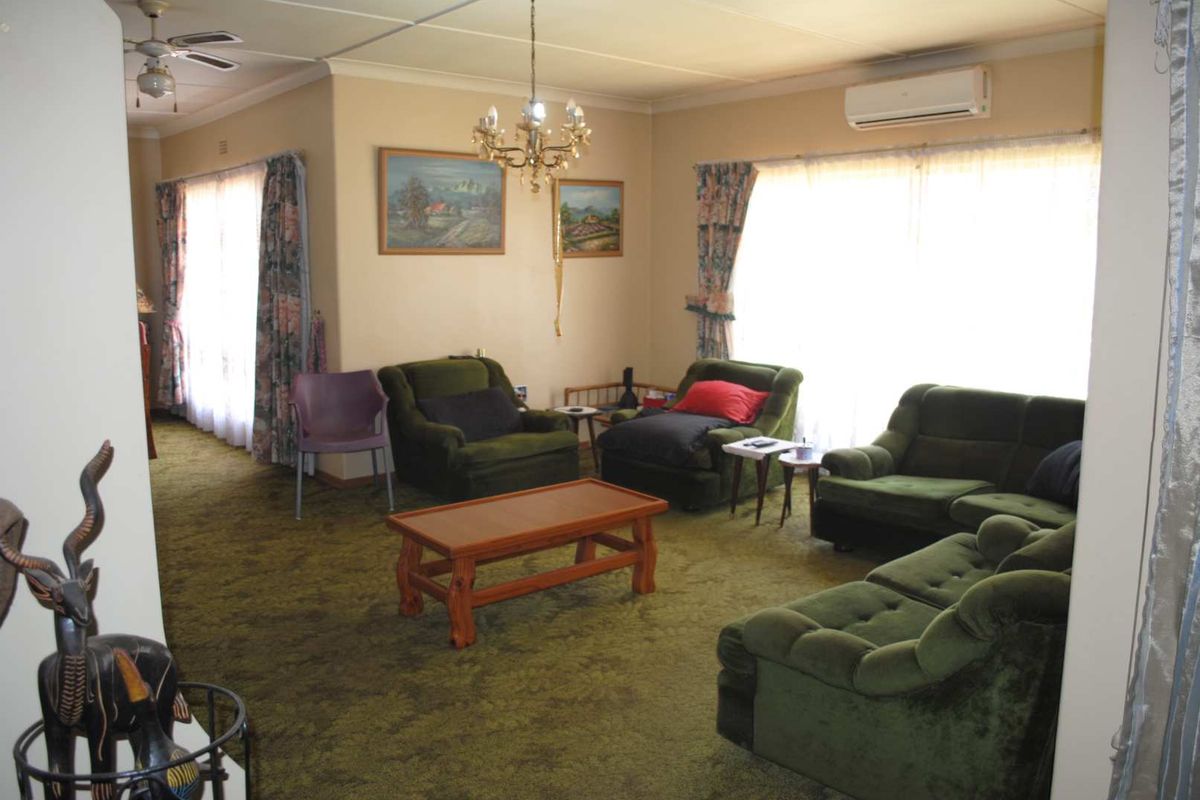 Spacious living room featuring carpet flooring, a ceiling fan, and a wall-mounted air conditioning unit, offering a comfortable and functional living space.