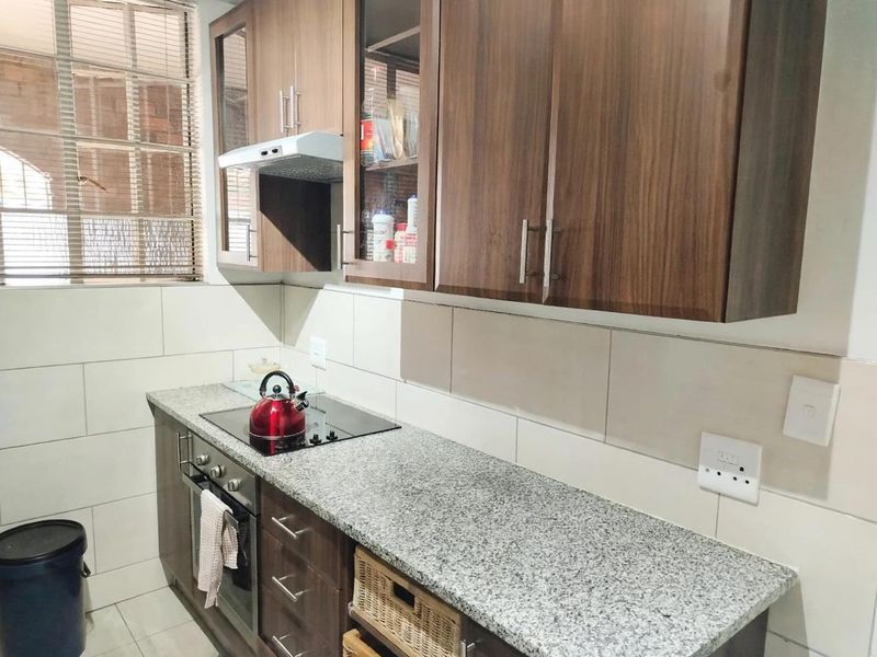 A functional kitchen featuring dark wood cabinetry, granite countertops, a built-in electric hob, oven, and a tiled backsplash.