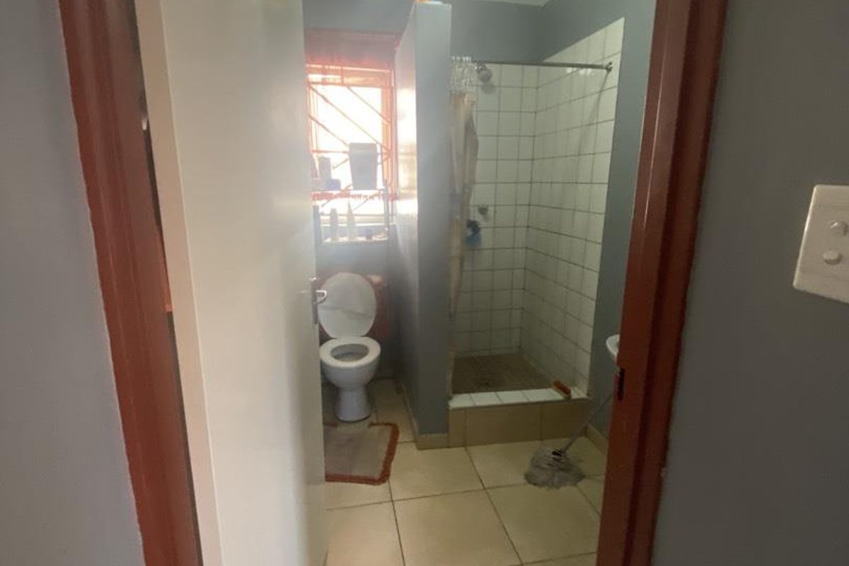A functional bathroom featuring a shower enclosure, toilet, and tiled finishes, viewed from the doorway.