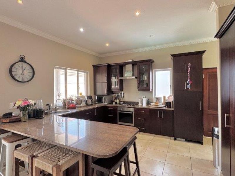 A well-appointed kitchen featuring dark wood cabinetry, granite countertops, a breakfast bar, and integrated appliances, complemented by tiled flooring and recessed lighting.