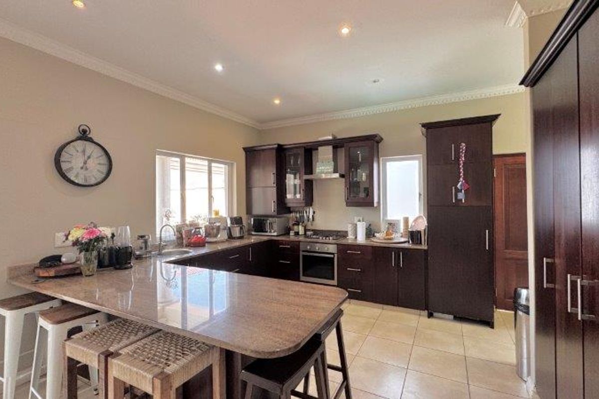 A well-appointed kitchen featuring dark wood cabinetry, granite countertops, a breakfast bar, and integrated appliances, complemented by tiled flooring and recessed lighting.